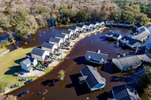 Aerial view of a flooded suburban neighborhood with multiple houses and vehicles surrounded by water.